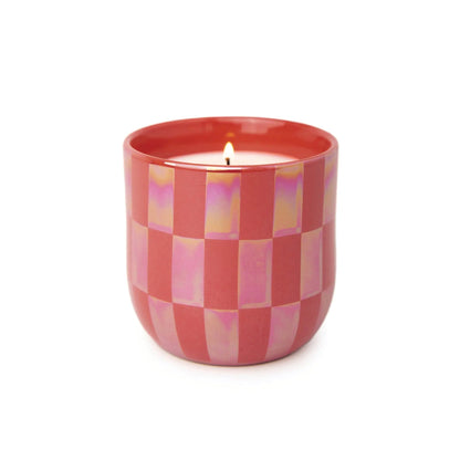 A lit Cactus Flower - Lustre Candle 10 oz glows in a pink, checkered ceramic holder against a white background.