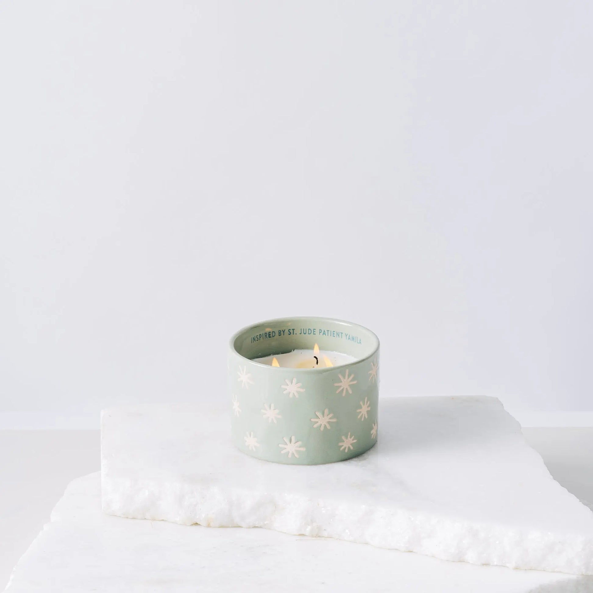 Green ceramic candle with sparkles and white soy wax center with three wicks burning 