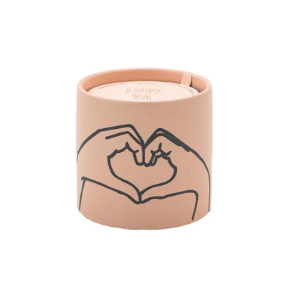 The Tobacco + Vanilla "Love Ya" - Impressions 5.75 oz Candle features a beige ceramic container with a minimalist line drawing of two hands forming a heart on its exterior.
