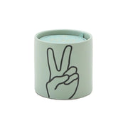 The Lavender + Thyme "Peace" Impressions 5.75 oz Candle comes in a light green cylindrical container featuring a minimalist black line drawing of a hand making a peace sign on the front.